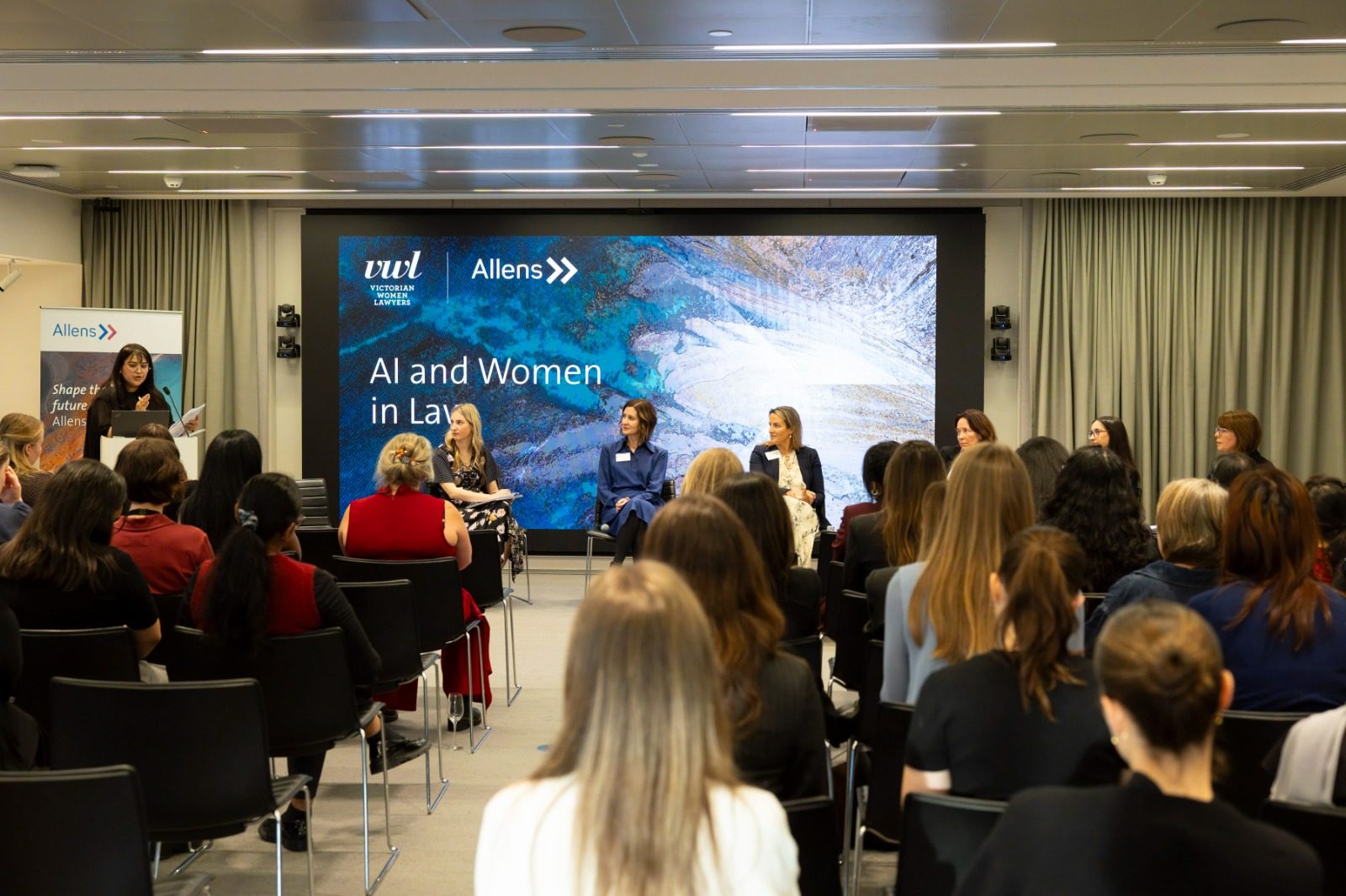 A panel discussion featuring several speakers seated in front of an audience, for "AI and Women in Law.